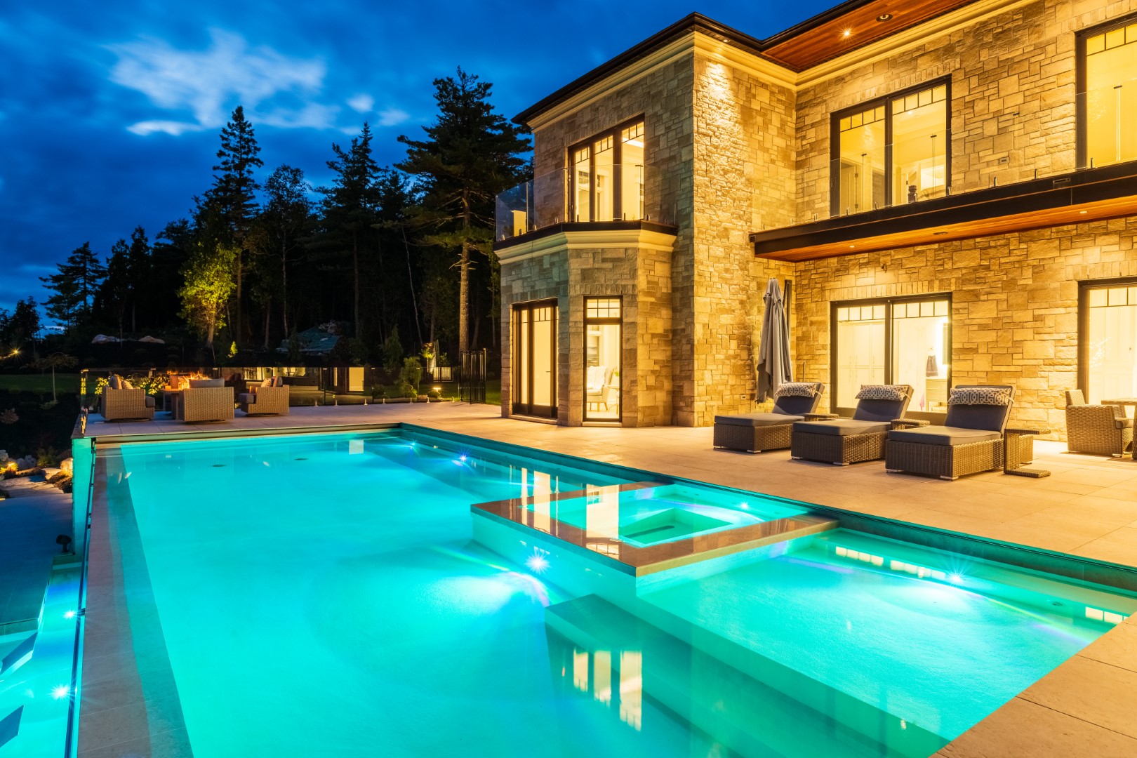 Luxury pool and hot tub with underwater lighting at night showing the back of home and garden in Saint John