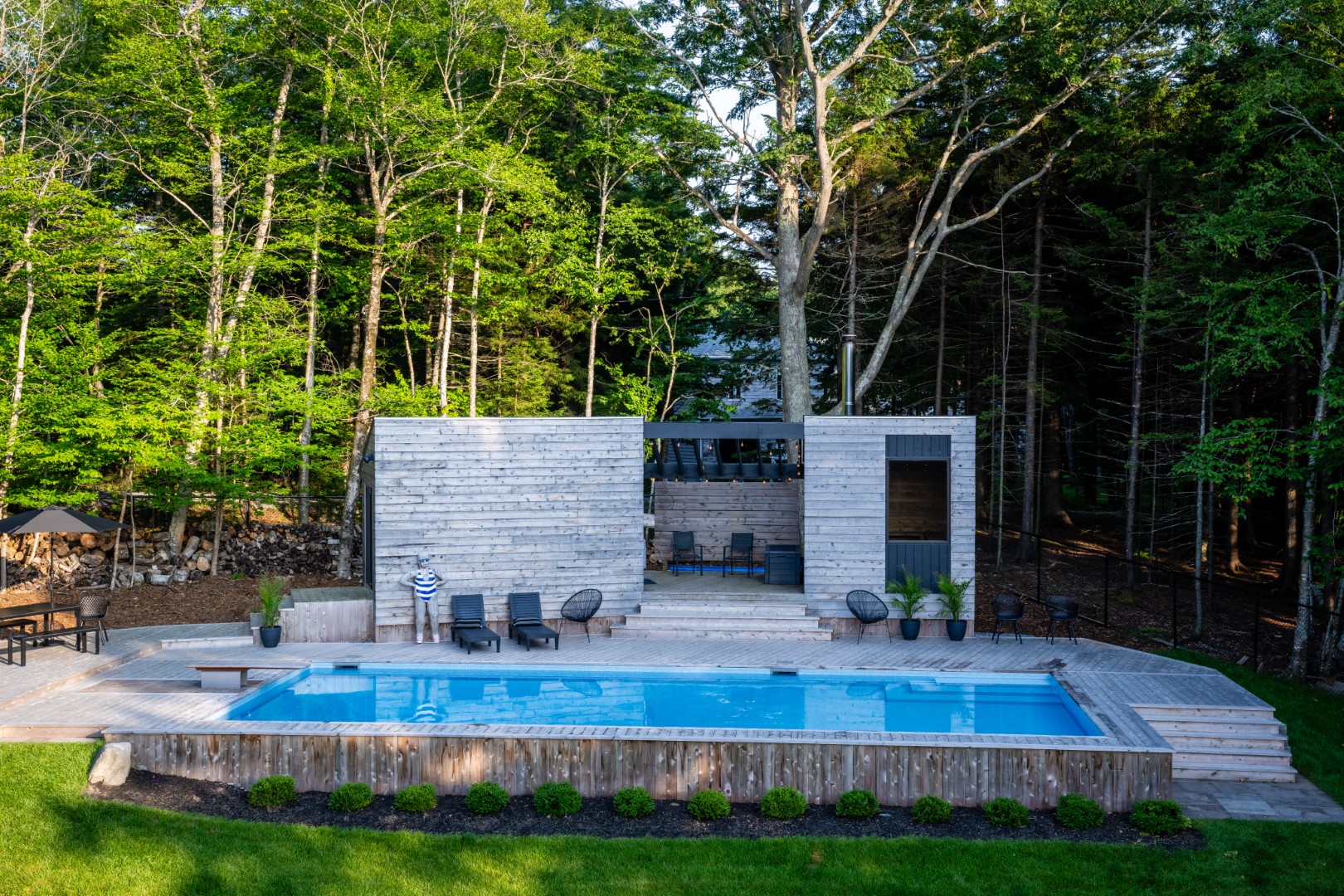 Wide shot of Pool with wooden diving board and modern wood patio in New Brunswick back garden