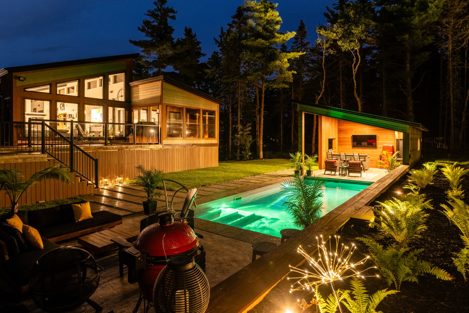 Wide view of home pool lit up with underwater lighting and the home and pool house in Lakeburn