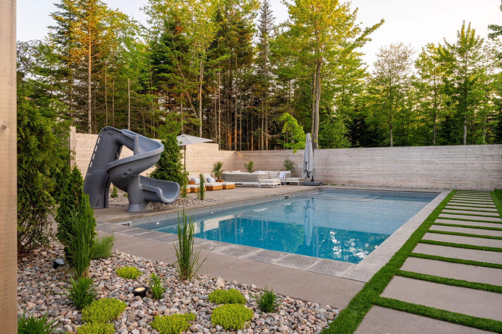 Pool with tanning ledge, slide and automatic pool cover in daytime in Moncton