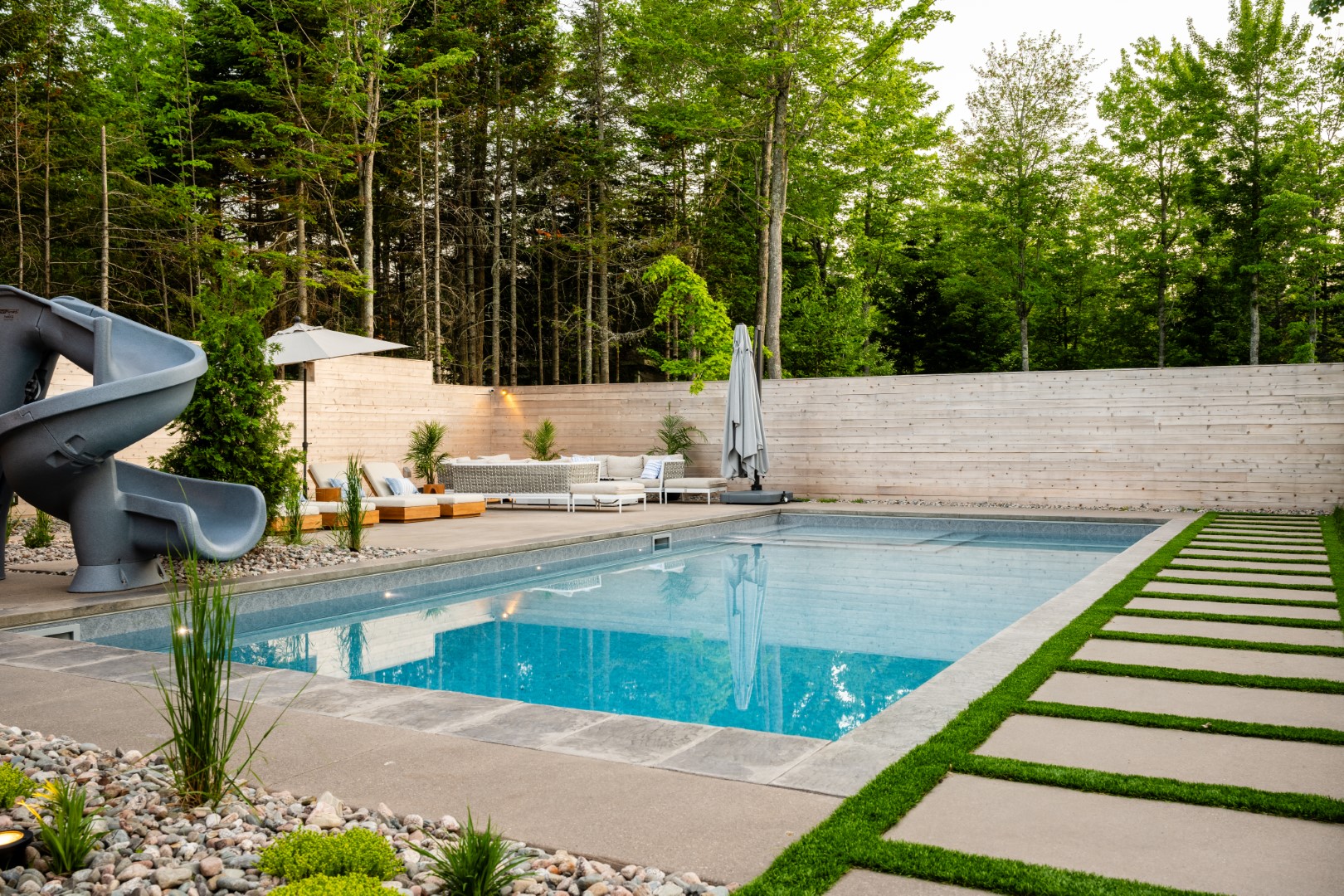 Daytime angled shot of Pool with tanning ledge, slide and automatic pool cover installed in Moncton home