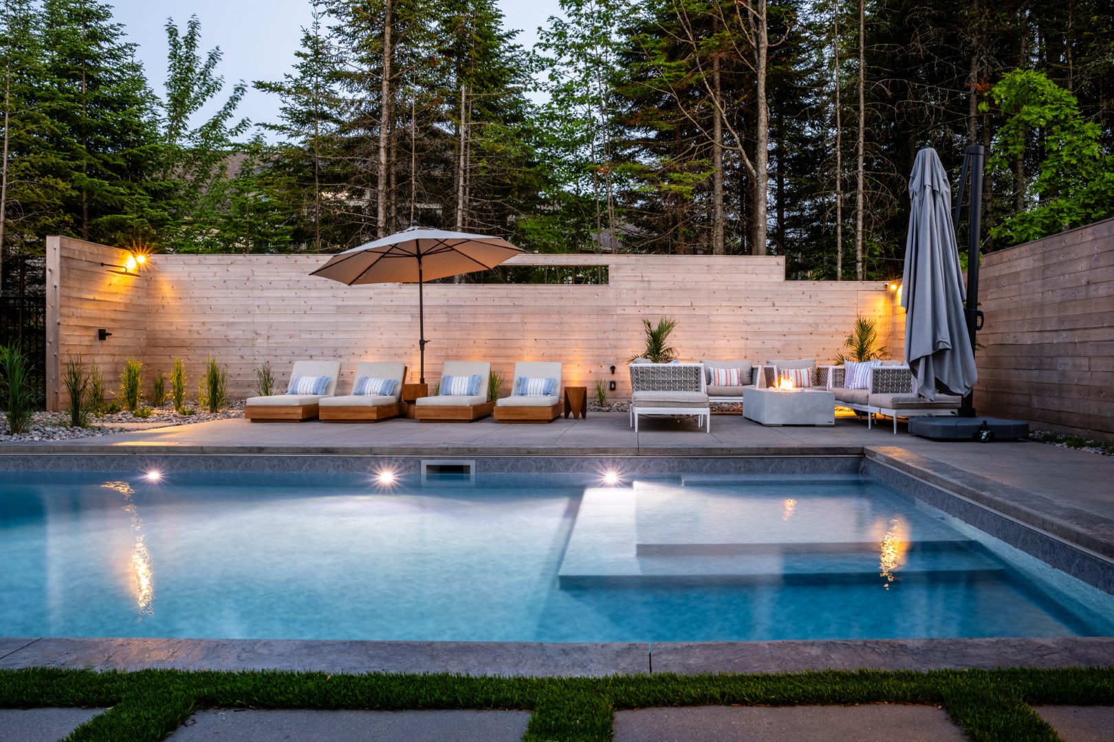 Seating area next to pool with tanning ledge and underwater lighting in Moncton home