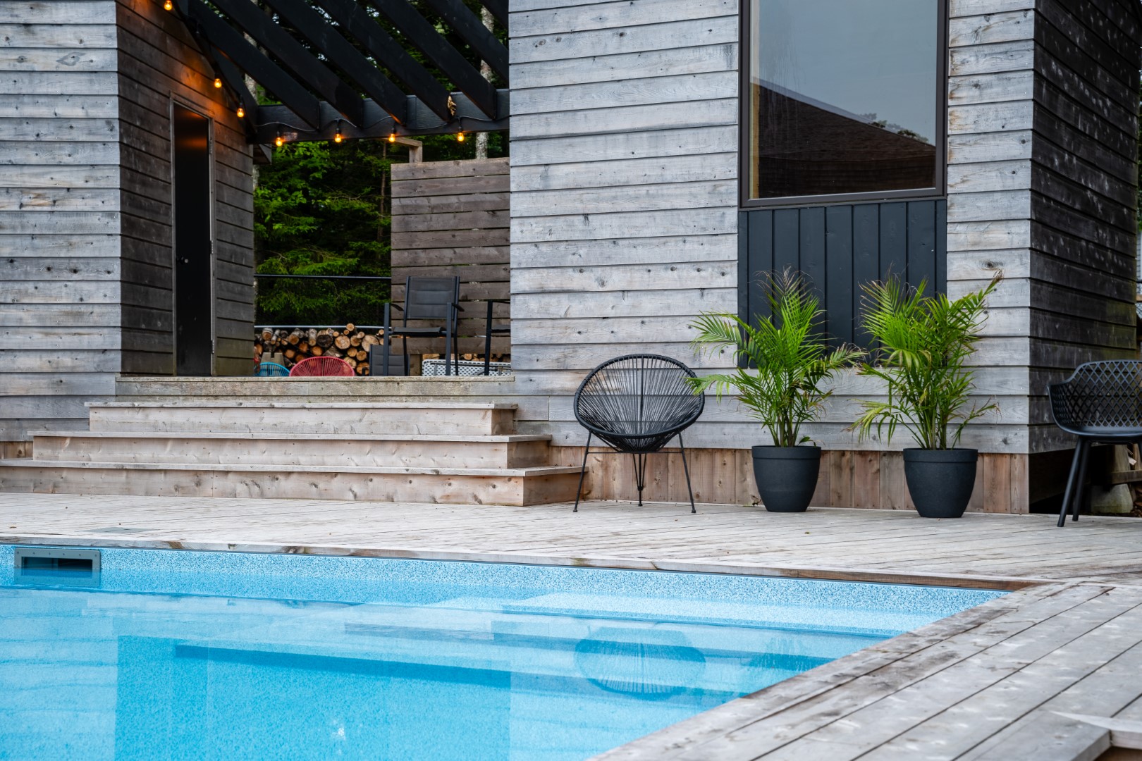 Pool with wooden diving board and modern wood patio in New Brunswick back garden