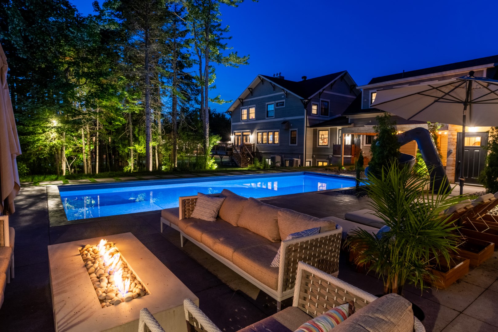 Pool with tanning ledge, slide and automatic pool cover at night with underwater lighting in Moncton