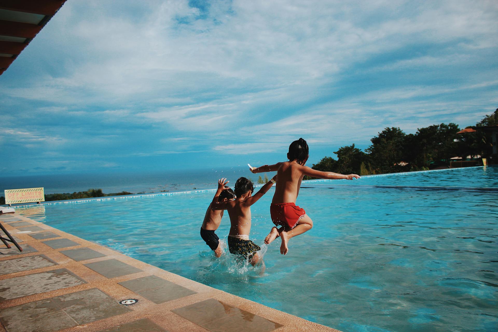 3 young boys diving into a pool to keep cool in sunny weather.
